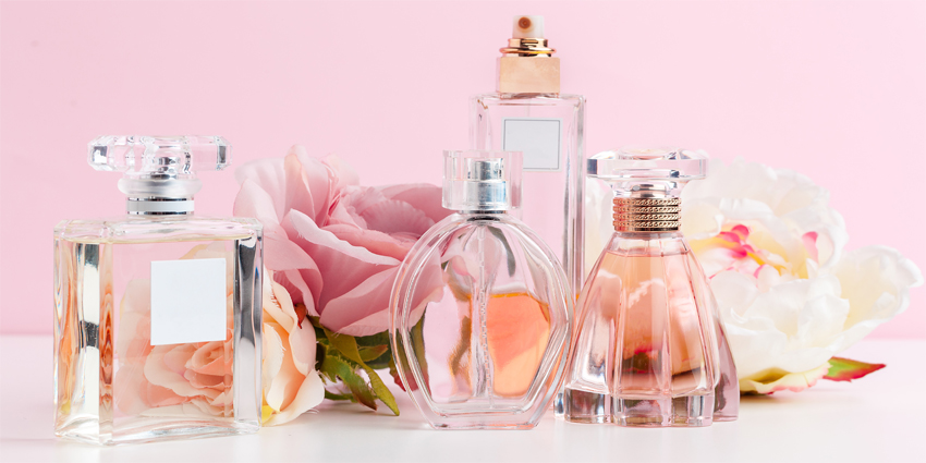 Bottle of perfume with flowers on color background